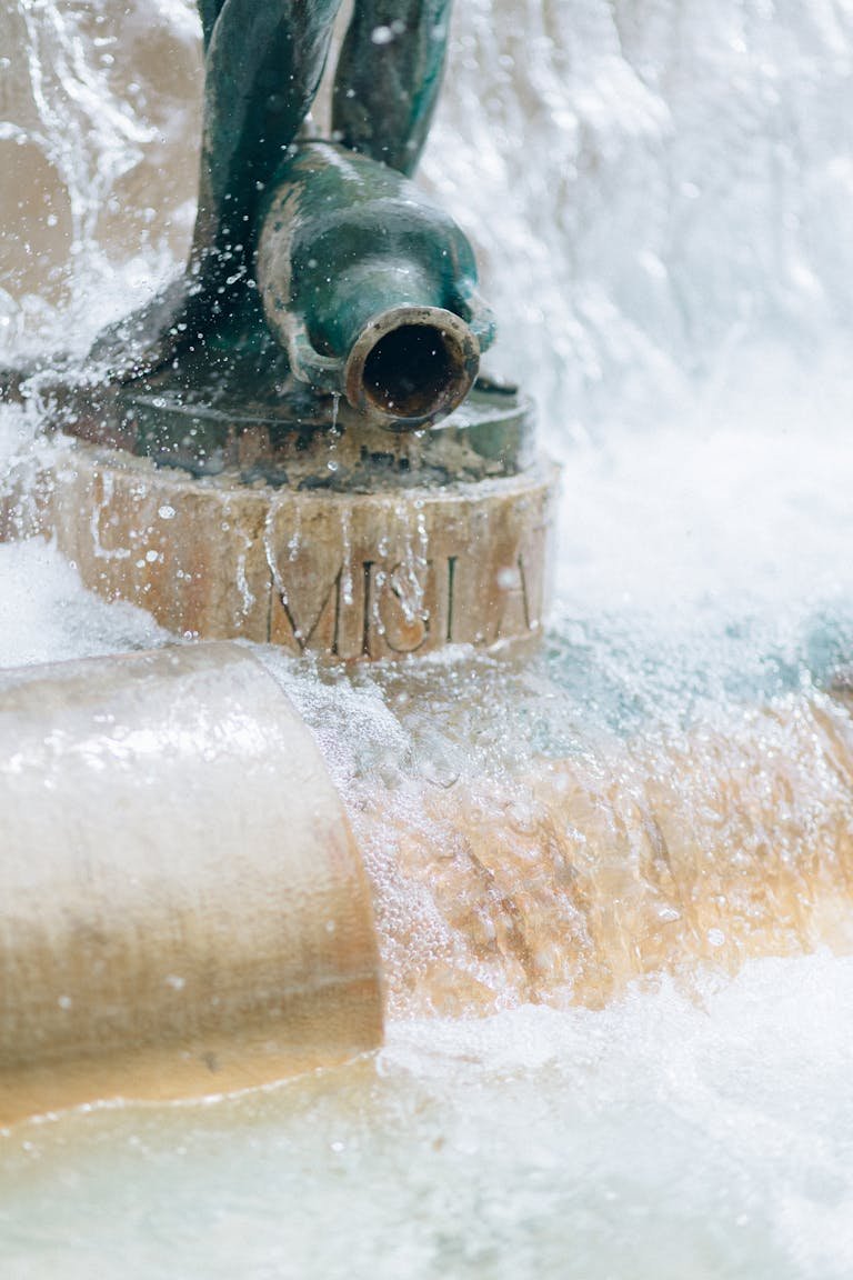 Close-up of water cascading from a fountain spout in an urban environment, creating a soothing spray.