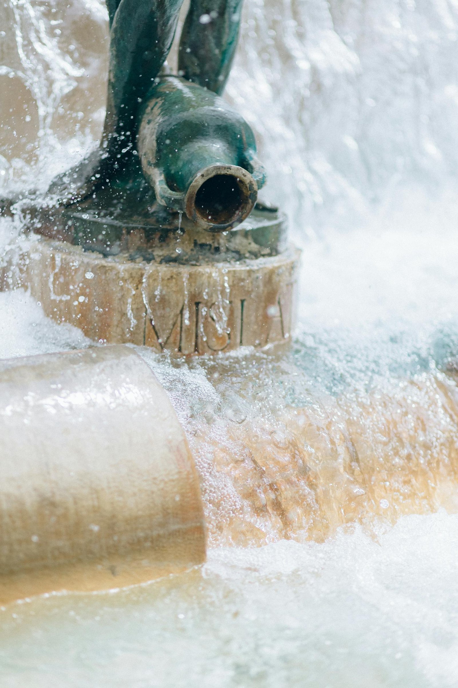 Close-up of water cascading from a fountain spout in an urban environment, creating a soothing spray.
