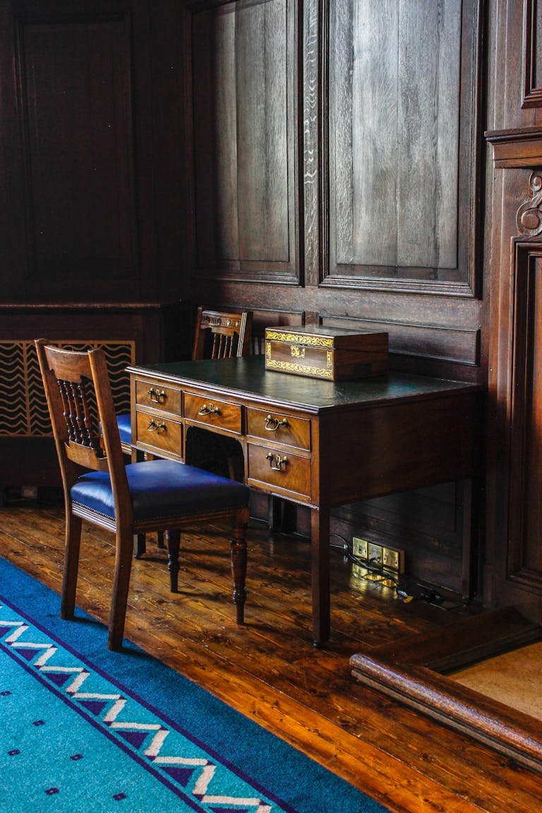 A beautifully captured vintage writing desk and chair set in a luxurious wooden paneled room.