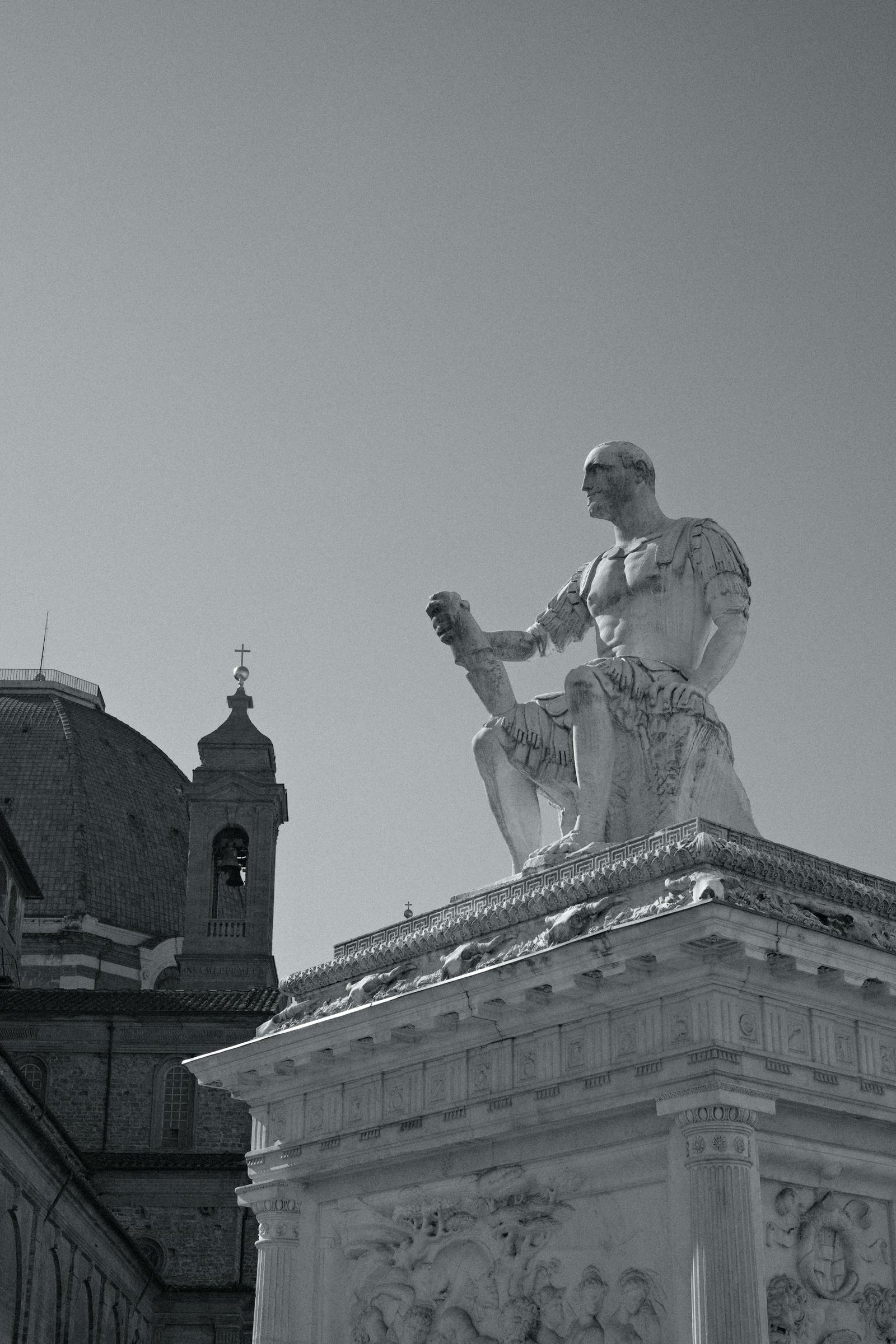 A striking black and white photo of a historical statue with architectural background.
