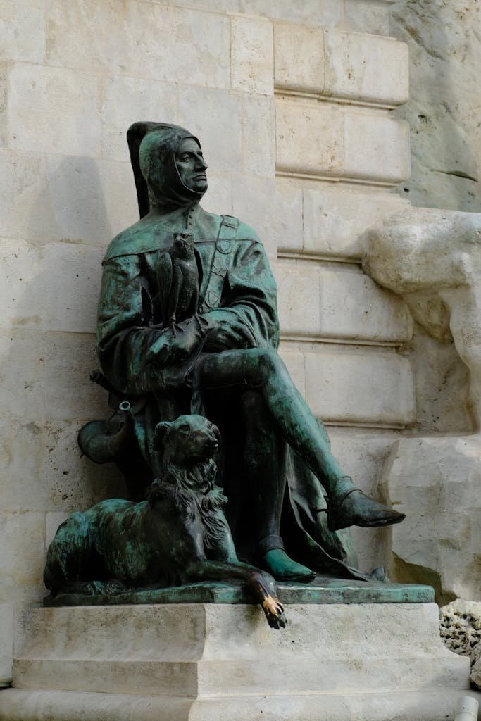 Bronze statue of a historical figure sitting with a dog, outdoor stone background.