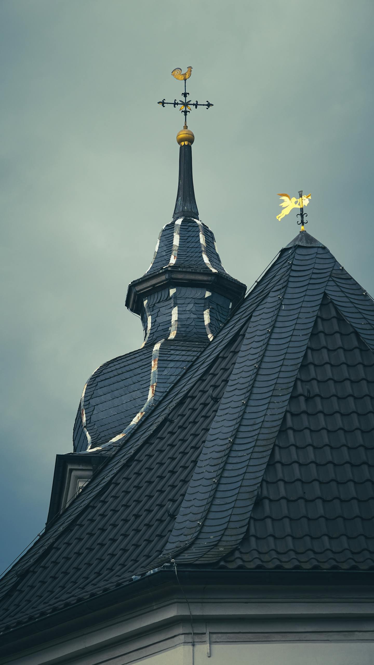 Close-up of an ornate European roof with a weather vane under cloudy skies.
