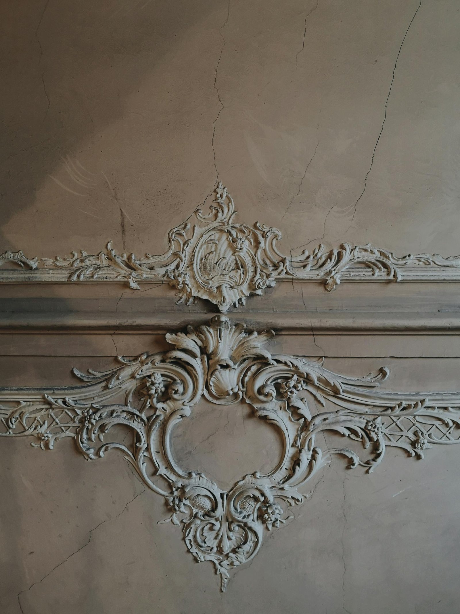 Close-up of weathered stucco wall with intricate ornamental design, showing vintage elegance and artistic craftsmanship.