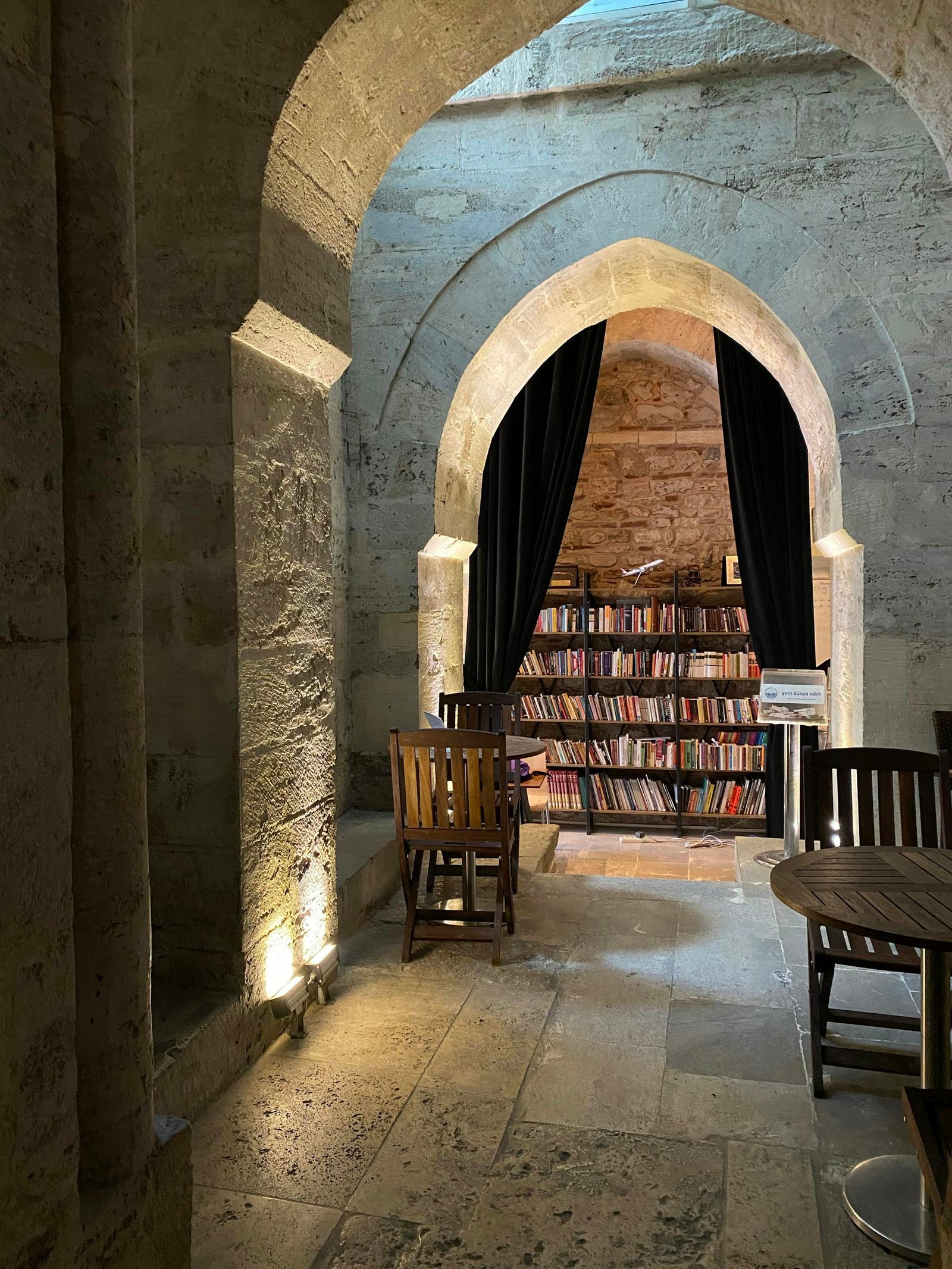 Cozy library nook with stone arches and wooden furniture, showcasing bookshelves in a historic setting.