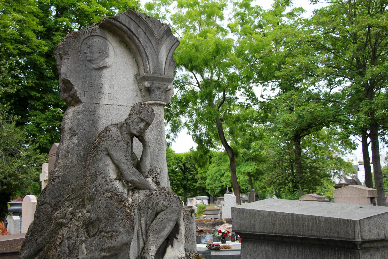 Elegant stone sculpture in a Paris cemetery surrounded by lush trees.