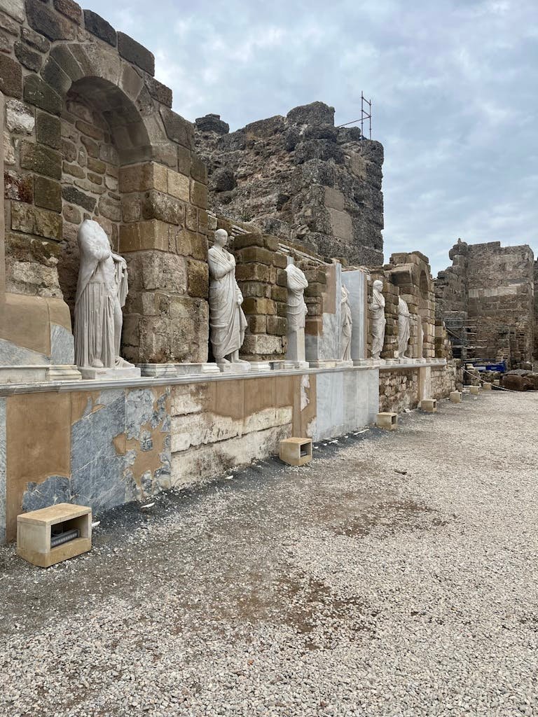 Explore ancient ruins adorned with classic sculptures under a cloudy sky.