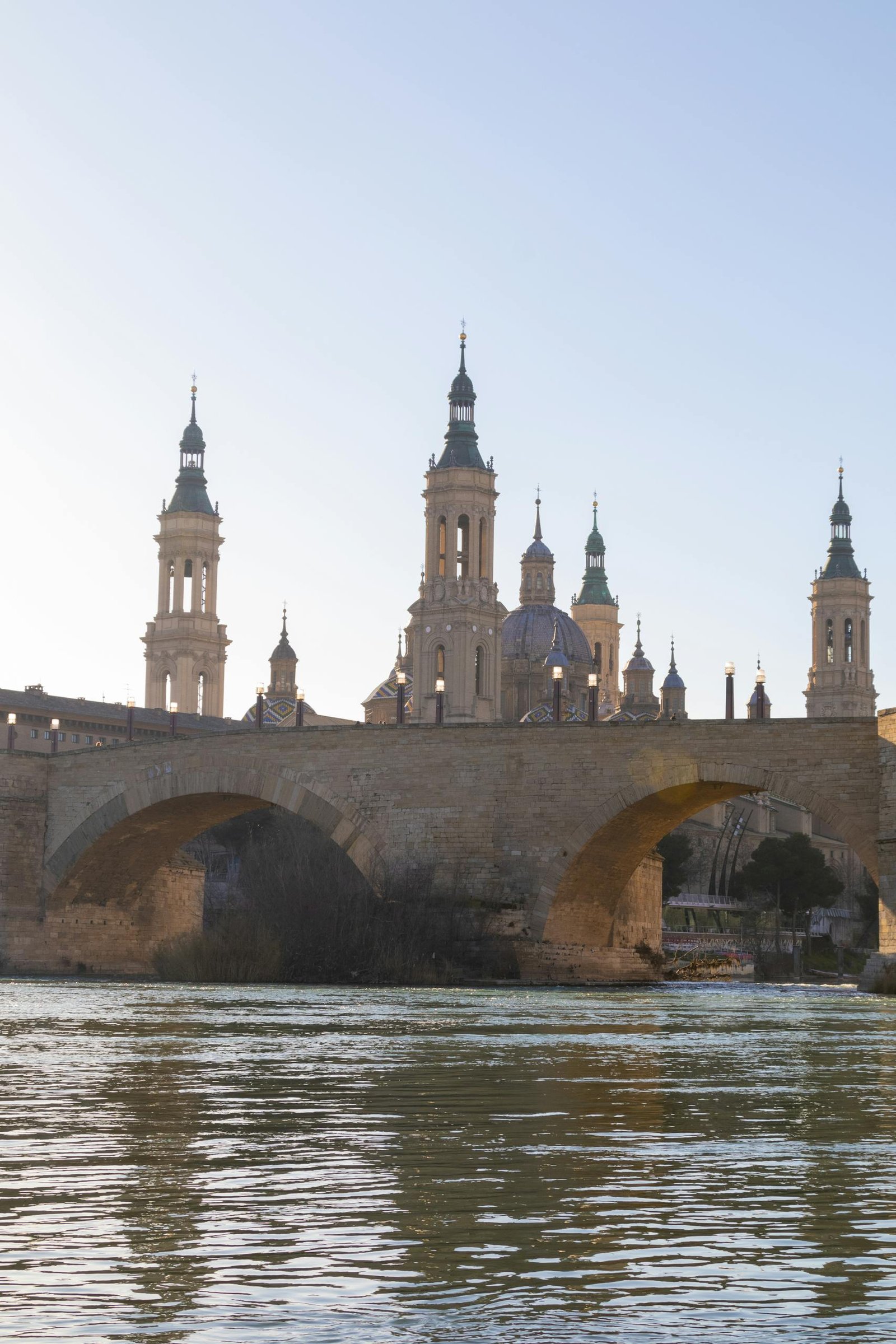 Historic Basilica of Our Lady of the Pillar with stone bridge at sunset in Zaragoza, Spain.