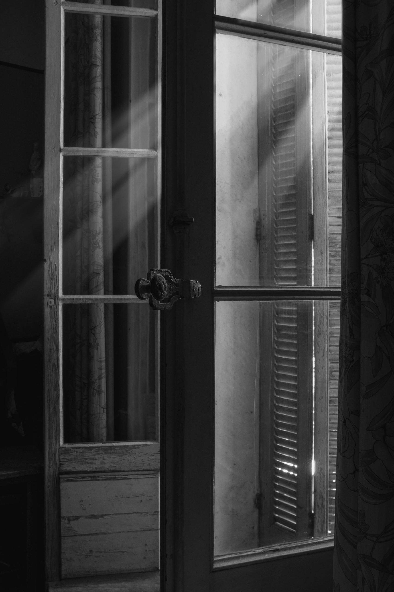 Sunlight filters through vintage French shutters, casting a serene glow in this black and white image.